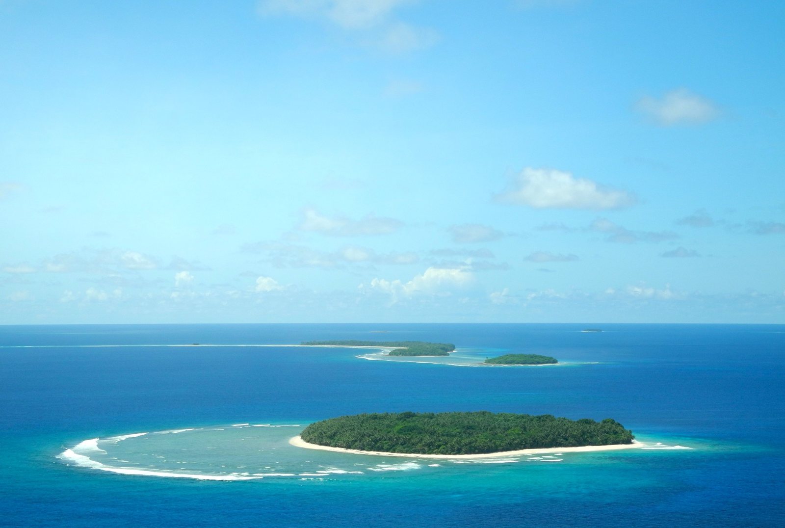 An aerial view of green islands, white beaches, reefs, and blue ocean.