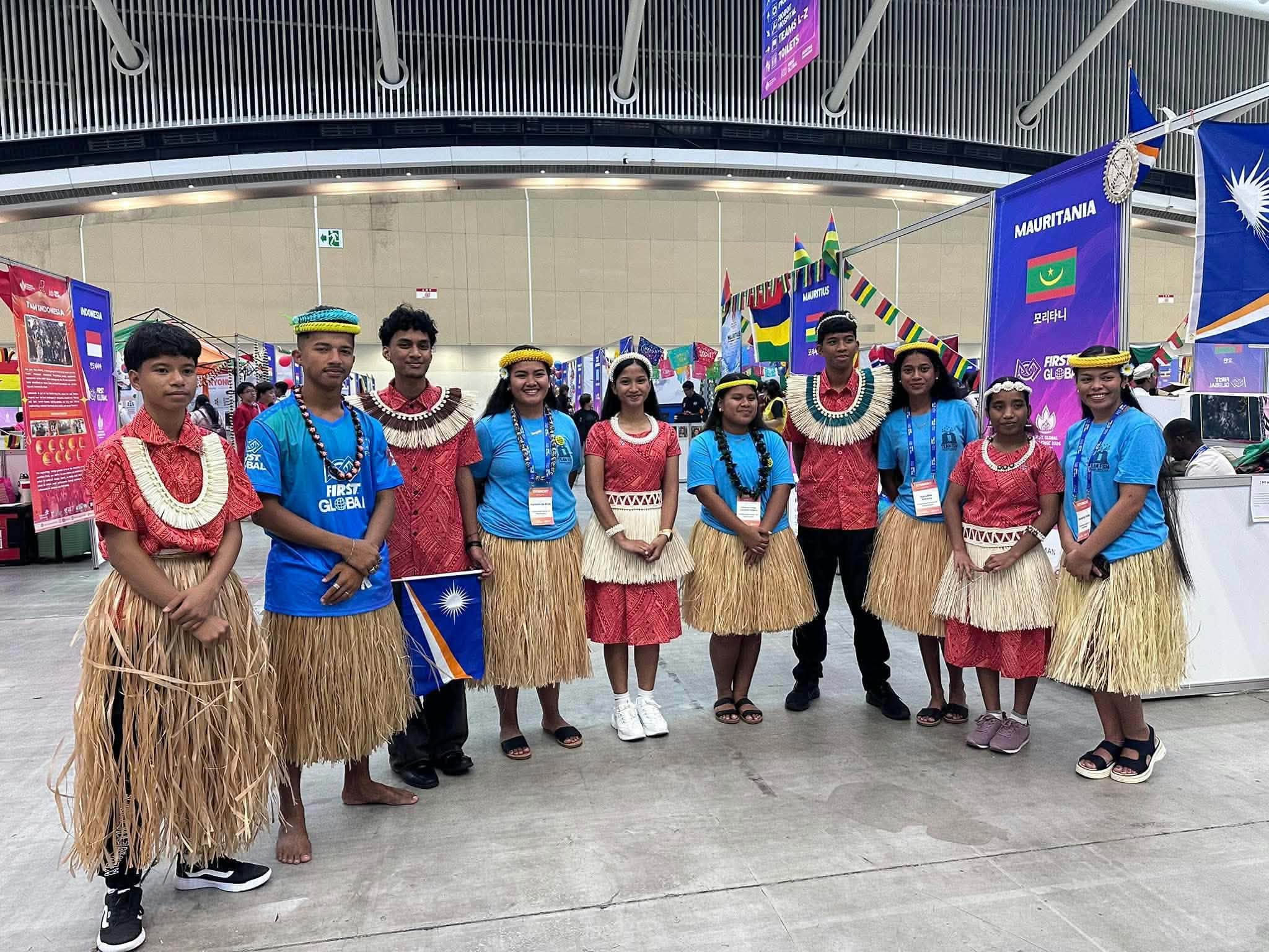 Team FSM members in blue shirts stand with fellow participants in red and woven attire at FIRST Global 2026.