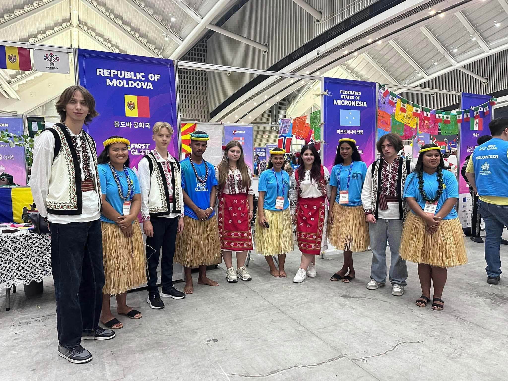 Team FSM poses with fellow FIRST Global participants in traditional attire beside the national team booths.
